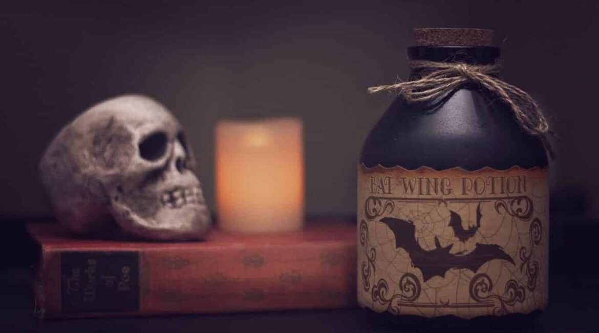 Bottiglia etichettata con pipistrelli, teschio su un libro e candela