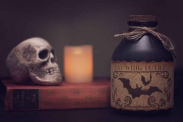 Bottiglia etichettata con pipistrelli, teschio su un libro e candela